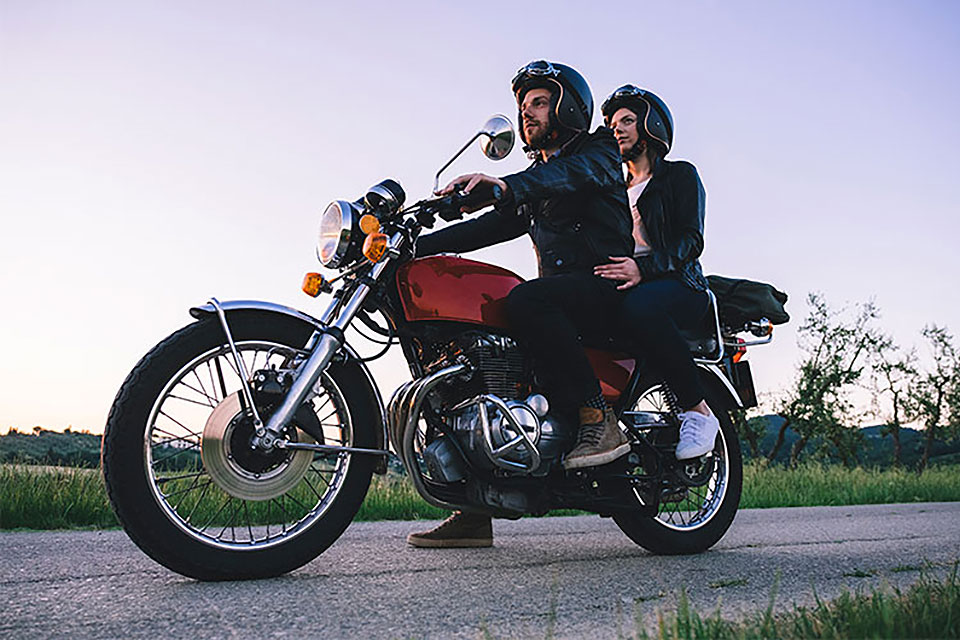 Eine Frau und ein Mann fahren mit einem Motorrad gemeinsam über eine Landstraße