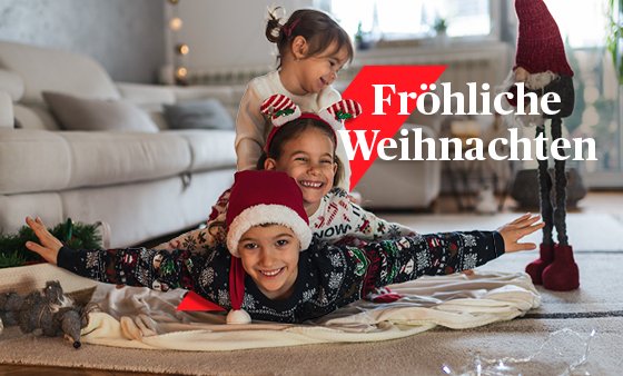 Drei kleine Kinder toben fröhlich am Weihnachtsabend. Eines der Kinder trägt eine rote Weihnachtsmannmütze.