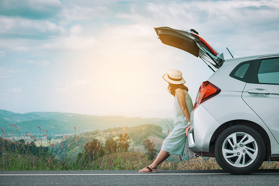 Eine junge Frau lehnt sich an ihr Auto und schaut sich den Sonnenaufgang an