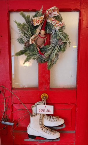 Weihnachtsgrüße AXA Bredstedt Volker Hassler-Risch Eine Rote Tür an der ein Weihnachtskranz hängt, sowie weiße Schlittschuhe.